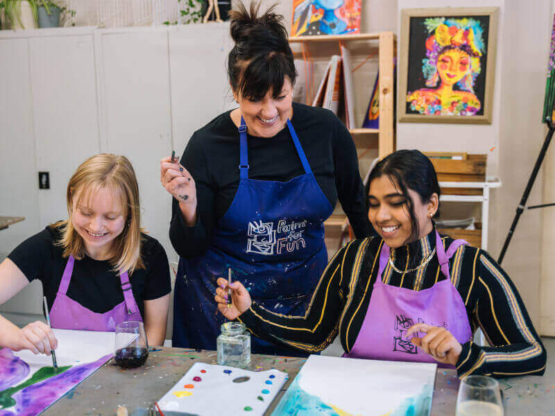 A couple are getting advice from a teacher at a paitning class as they add colour to a canvas.